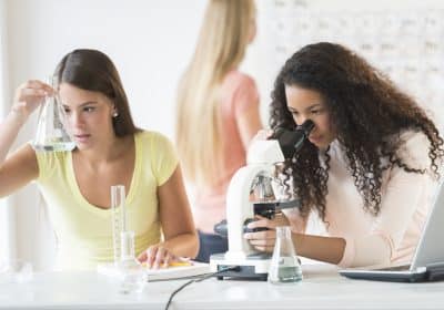 Teenage girls experimenting in chemistry class with friend in background