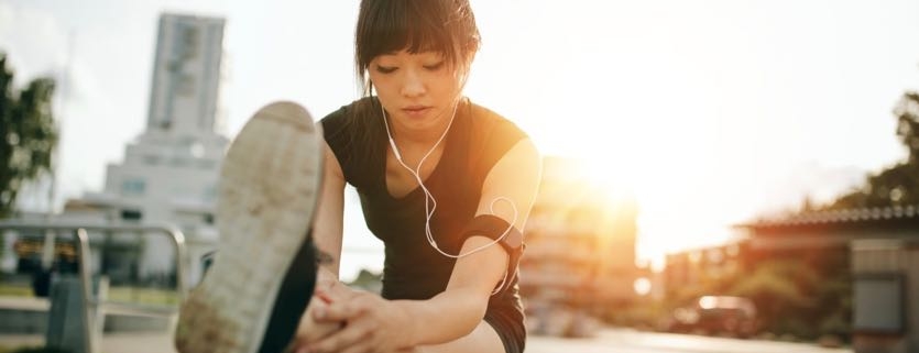 Shot of female runner stretching legs before her workout. Woman warming up before outdoor workout with sun flare.