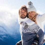 Loving couple playing together in snow outdoor. Winter holidays in mountains. Man and woman wearing knitted clothing having fun on weekends.
