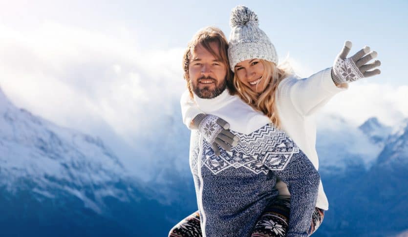 Loving couple playing together in snow outdoor. Winter holidays in mountains. Man and woman wearing knitted clothing having fun on weekends.