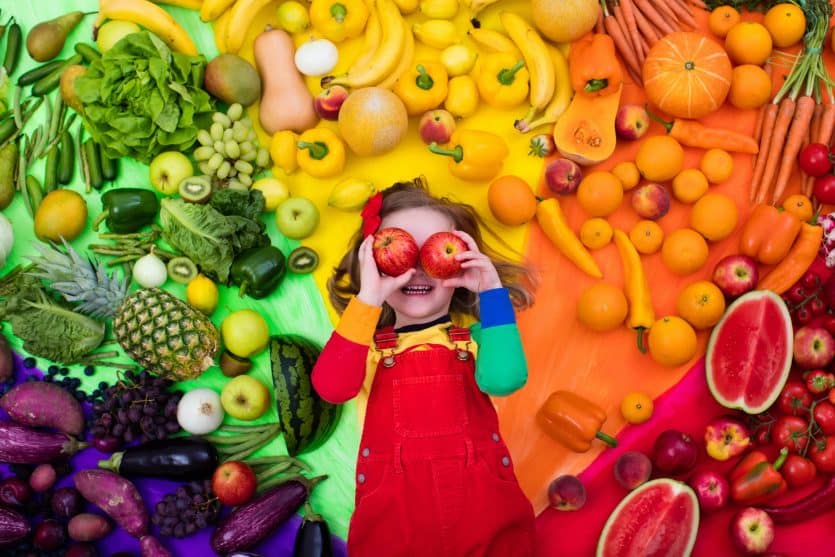 Little girl with variety of fruit and vegetable. Colorful rainbow of raw fresh fruits and vegetables. Child eating healthy snack. Vegetarian nutrition for kids. Vitamins for children. View from above.