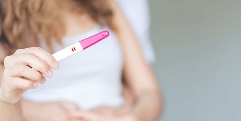 Selective focus happy couple hugging with positive pregnancy test in bedroom.