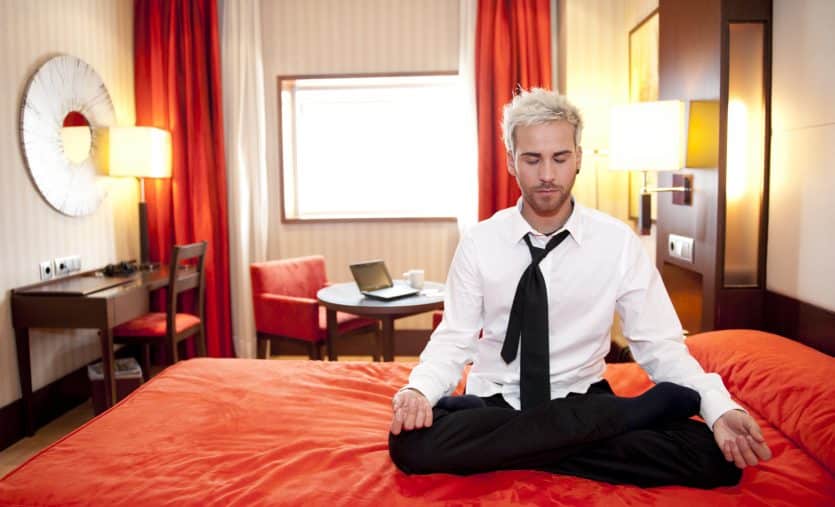 Caucasian businessman meditating in bed in lotus position.