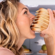 Close-up Of A Hungry Woman Eating Sandwich Near Refrigerator