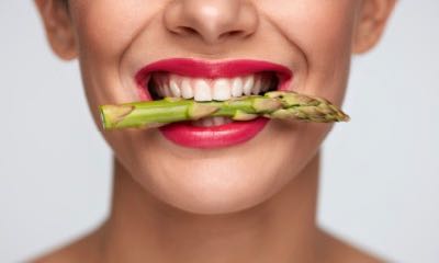 Healthy Eating. Closeup Of Woman Mouth With Beautiful Pink Lips Makeup Holding Fresh Asparagus Between White Teeth. Smiling Female Face With Vegetable In Mouth. Diet Food Concept. High Resolution