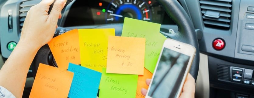 To do list in a car on driving wheel and hand holding phone - busy day concept