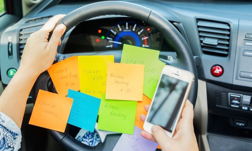 To do list in a car on driving wheel and hand holding phone - busy day concept