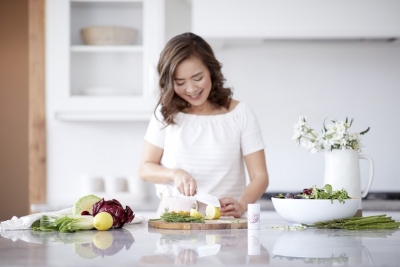 woman in kitchen slicing lemons surrounded by healthy foods and a bottle of EstroPro on counter