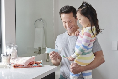 father holding young daughter putting toothpaste on brush